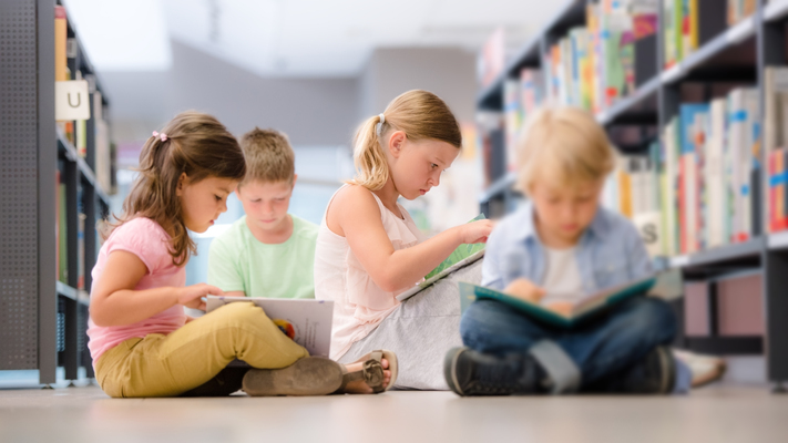 Un grupo de niños sentados en una biblioteca leyendo libros