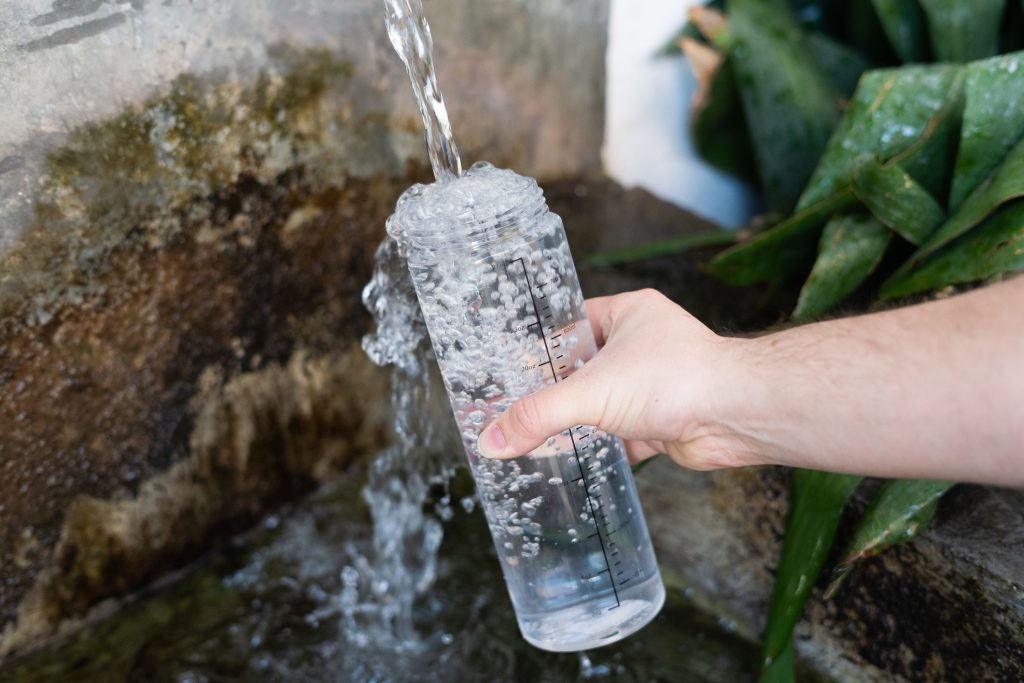 unrecognizable-man-refilling-a-water-bottle-at-a-natural-fountain