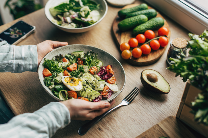 woman-mixing-delicious-superfood-salad-ingredients-with-wooden-spoons-in-kitchen