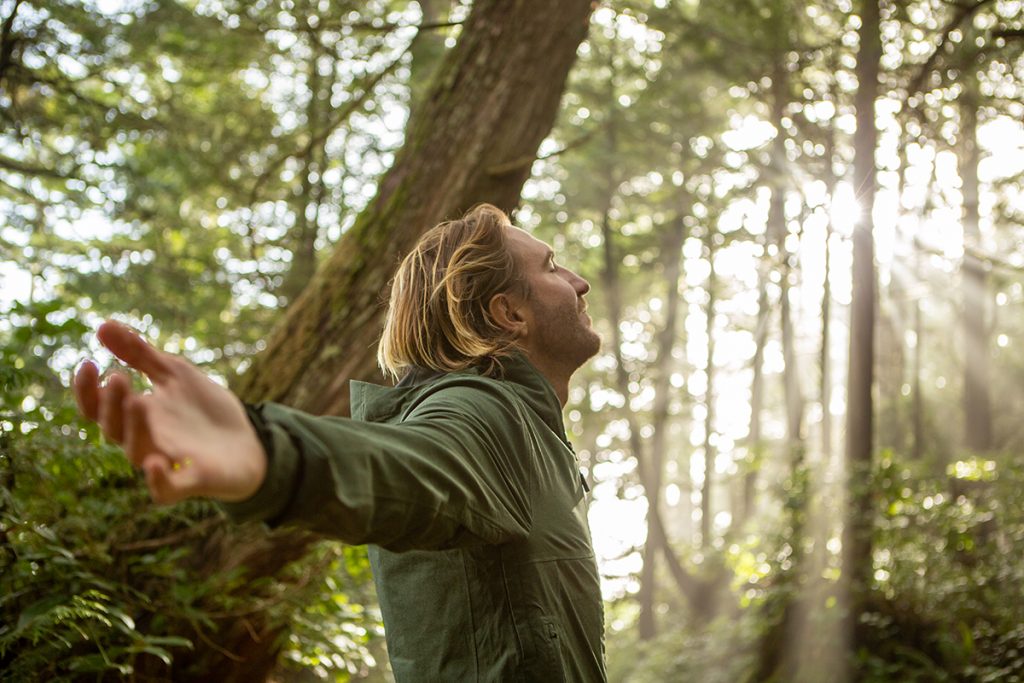 young-man-embracing-rainforest-standing-in-sunbeams-illuminating-the-trees